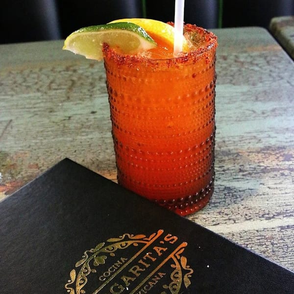 A vibrant orange Margarita's Cocina Mexicana cocktail with lime and a chili-salt rim on a rustic table.