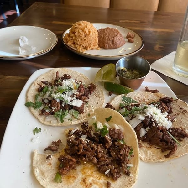 Three carne asada tacos with cilantro, onions, and cheese, served with rice and beans.
