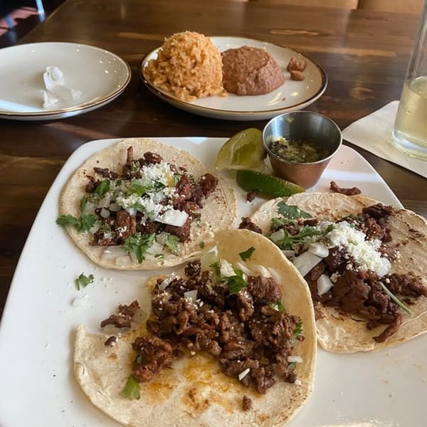 Three Margarita's Cocina Mexicana street tacos with rice, beans, lime, and salsa on a wooden table.