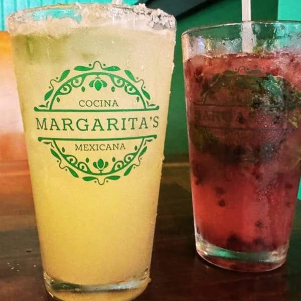 Two drinks, a Margarita's Cocina Mexicana margarita and a berry mojito, on a dark table.