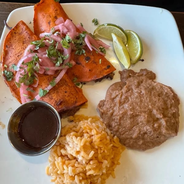 Three red birria tacos with pickled onions, cilantro, limes, rice, refried beans, and dipping sauce.