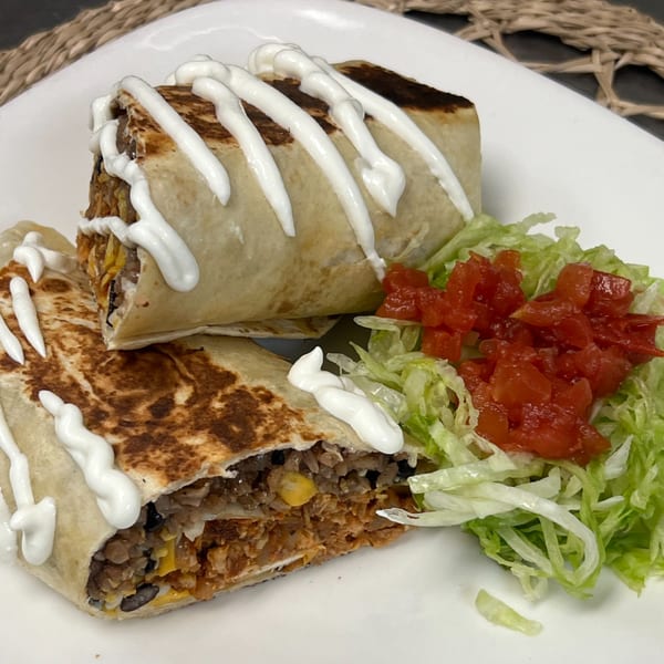 Two burritos drizzled with sour cream, served with shredded lettuce and diced tomatoes.