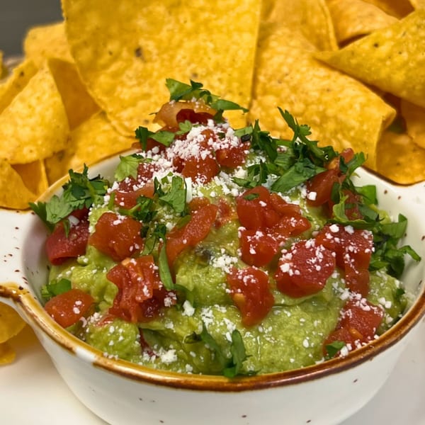A bowl of guacamole topped with diced tomatoes, crumbled cheese, and cilantro, with tortilla chips.