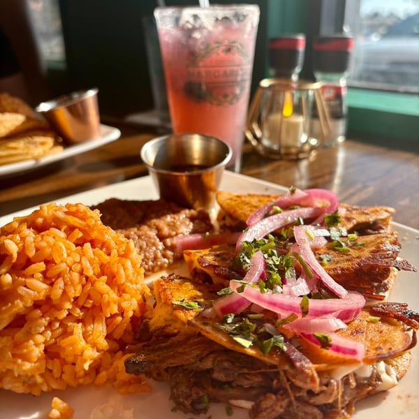 Mexican dish with rice, beans, quesadillas topped with pickled onions, and a pink drink.