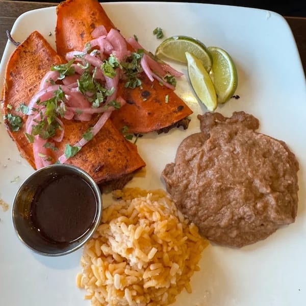 Three birria tacos with pickled onions, cilantro, limes, refried beans, rice, and a side of consommé.