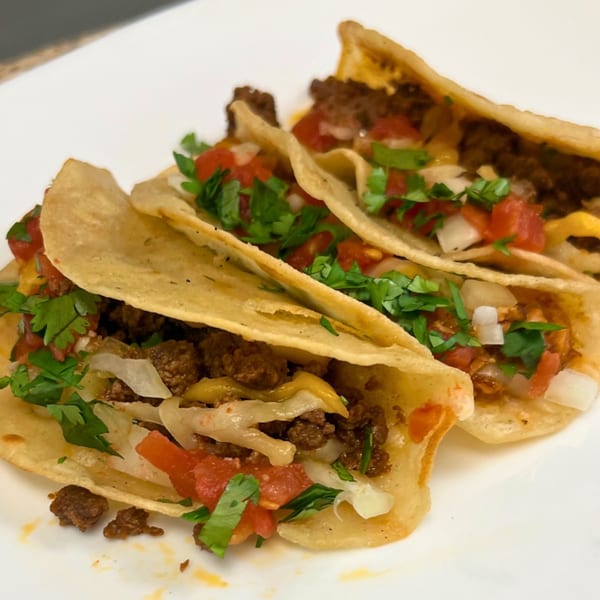 Three Margarita's Cocina Mexicana tacos filled with ground beef, cheese, diced tomatoes, onions, and cilantro.