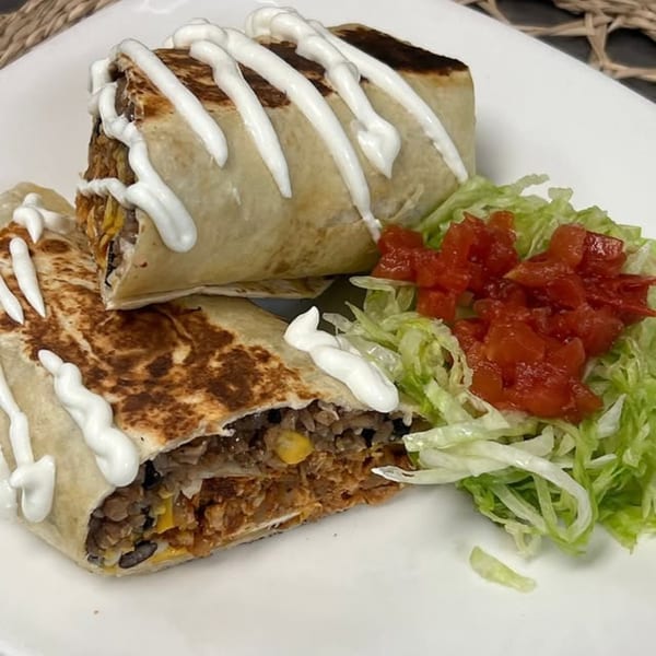 Two burritos topped with sour cream, served with shredded lettuce and diced tomatoes on a white plate.
